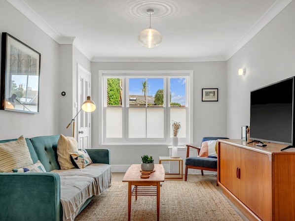A modern living room with a sofa, a coffee table, a TV, and a large window with a view of greenery.