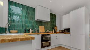 A modern kitchen with white cabinets, a wooden countertop, a green-tiled backsplash, and a built-in oven. - Charming cottage in the Heart of Whitstable - Pass the Keys (Whitstable)