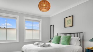 A bedroom with a bed, two windows, a hanging light fixture, a framed picture on the wall, and a bedside table with a lamp. - Charming cottage in the Heart of Whitstable - Pass the Keys (Whitstable)
