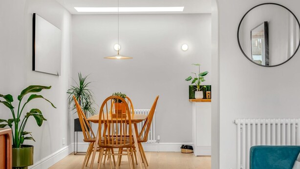 A modern living room with a dining area, featuring a wooden dining table, chairs, a sofa, and a circular mirror on the wall. - Charming cottage in the Heart of Whitstable - Pass the Keys (Whitstable)