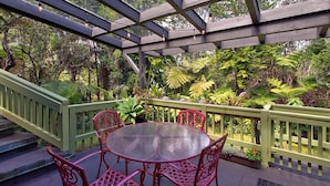 A covered outdoor seating area with a round table and chairs, surrounded by lush greenery and a wooden pergola. - Halehikiola: 1  BR, 2  BA House in Volcano, Sleeps 6 (Volcano)