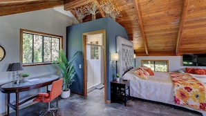 A bedroom with a bed, a desk, and a chair. There is a door leading to another room. - Halehikiola: 1  BR, 2  BA House in Volcano, Sleeps 6 (Volcano)