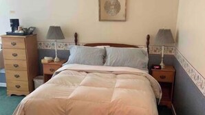 Un lit bien fait, avec une tête de lit en bois, deux tables de chevet avec des lampes, une commode et un tableau encadré accroché au mur.