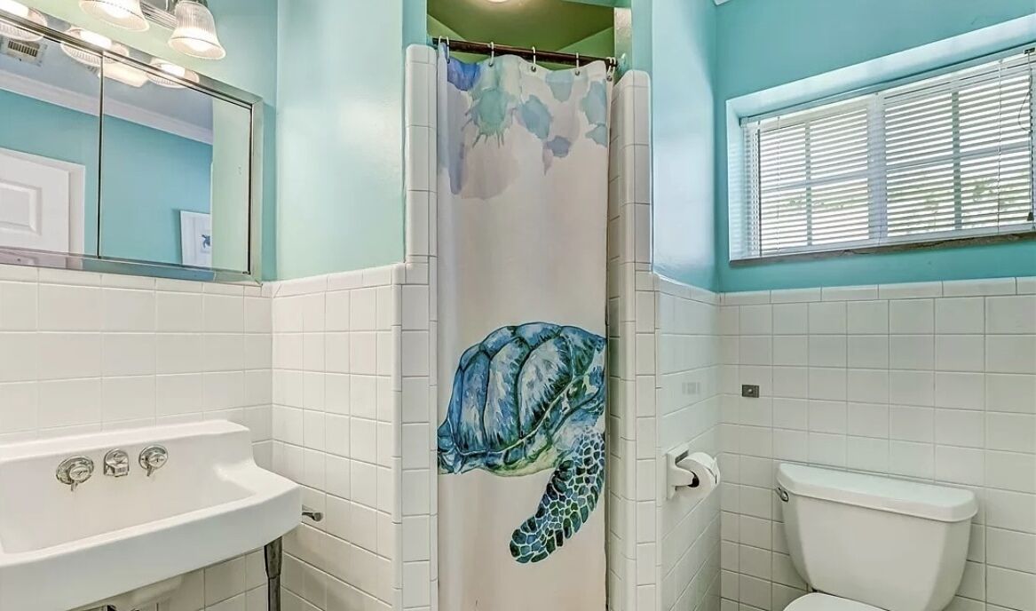 Une salle de bain avec un lavabo blanc, des toilettes et un rideau de douche orné d’un motif de tortue de mer.