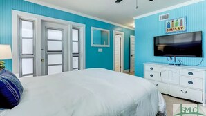 Un dormitori amb llit, ventilador de sostre, televisió i commode.