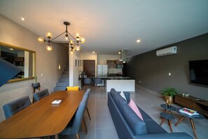 A modern living room with a wooden dining table, blue sofas, and a kitchen in the background.