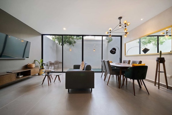 A modern living room with a sofa, dining table, chairs, and a TV.