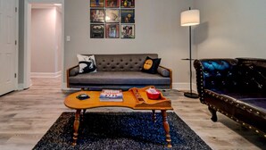 Un salón con un sofá gris, una mesa de centro de madera, un sofá de cuero negro y una pared con cuadros enmarcados.