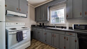 Una cocina con gabinetes grises, una estufa blanca, un lavamanos y un microondas.