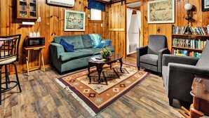 A cozy living room with wooden walls, a sofa, a coffee table, a bookshelf, and a television.