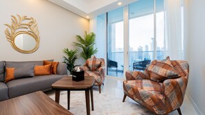 A modern living room with a grey sofa, a wooden coffee table, and two patterned armchairs. A decorative mirror and a potted plant are also visible. - GLOBALSTAY. New Apartments in Business Bay (Dubai)