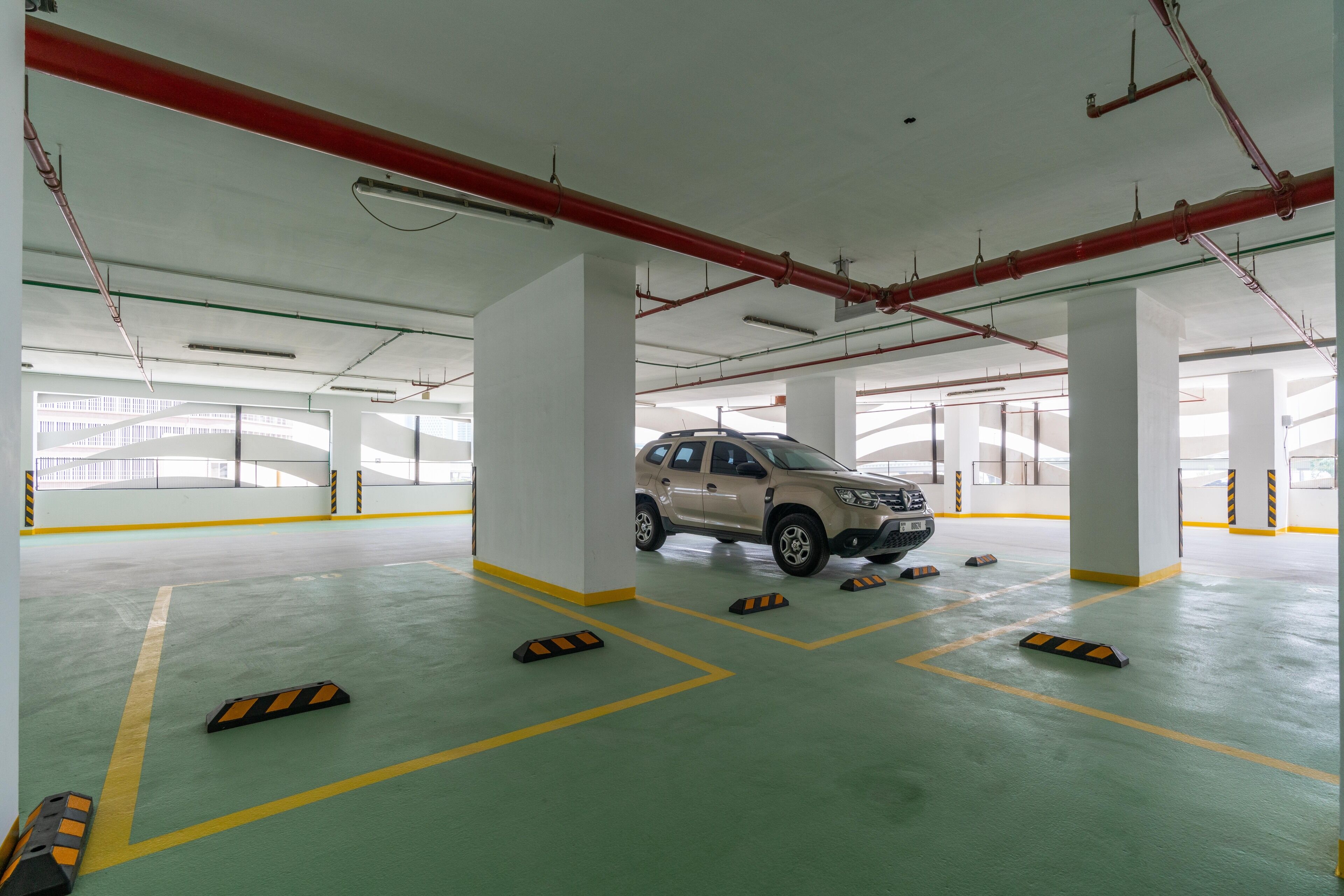 Eine geräumige Parkgarage mit mehreren Ebenen, sichtbaren Deckenrohren und einem beige farbenen SUV.