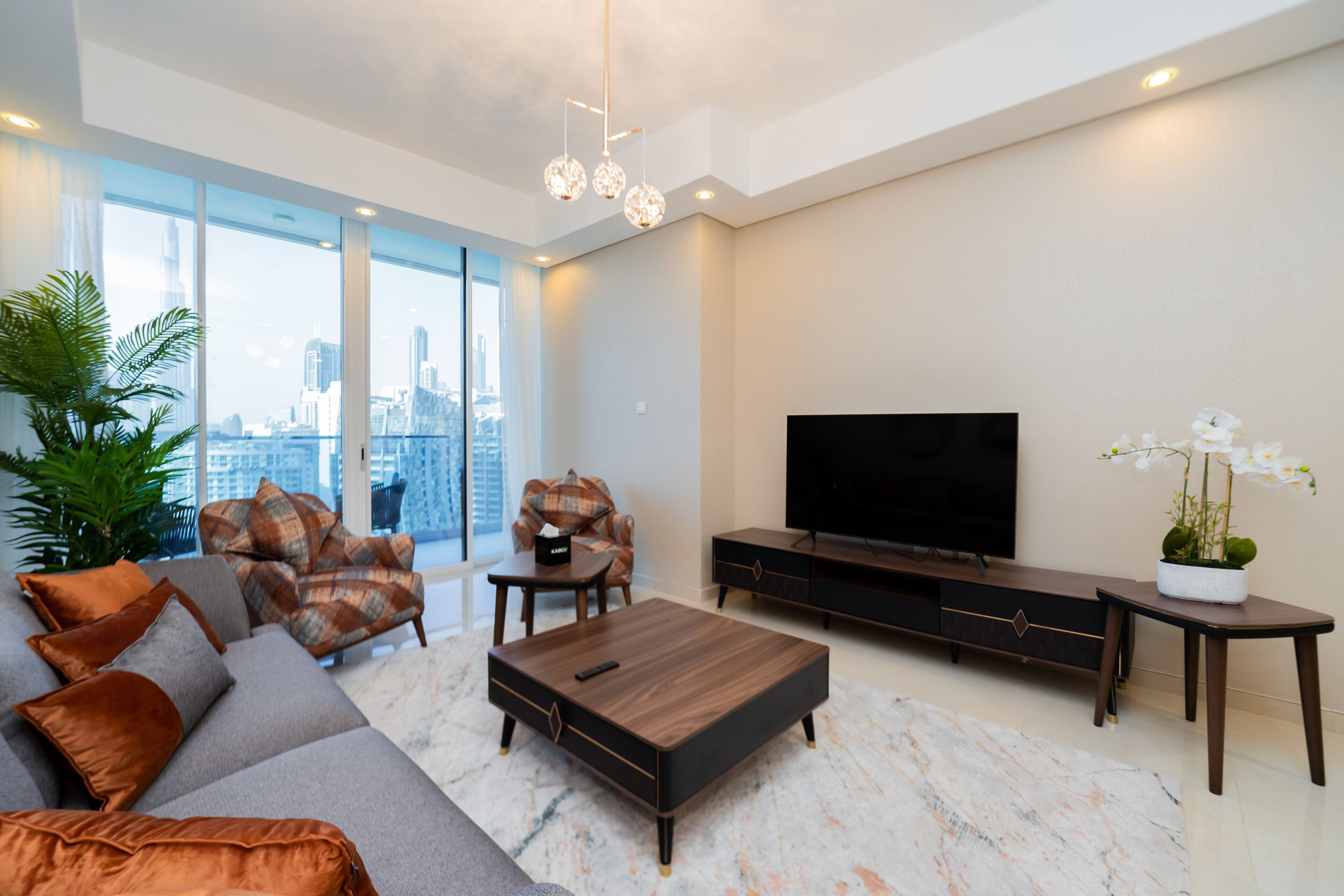 A modern living room with a large TV, comfortable seating, and a city view.