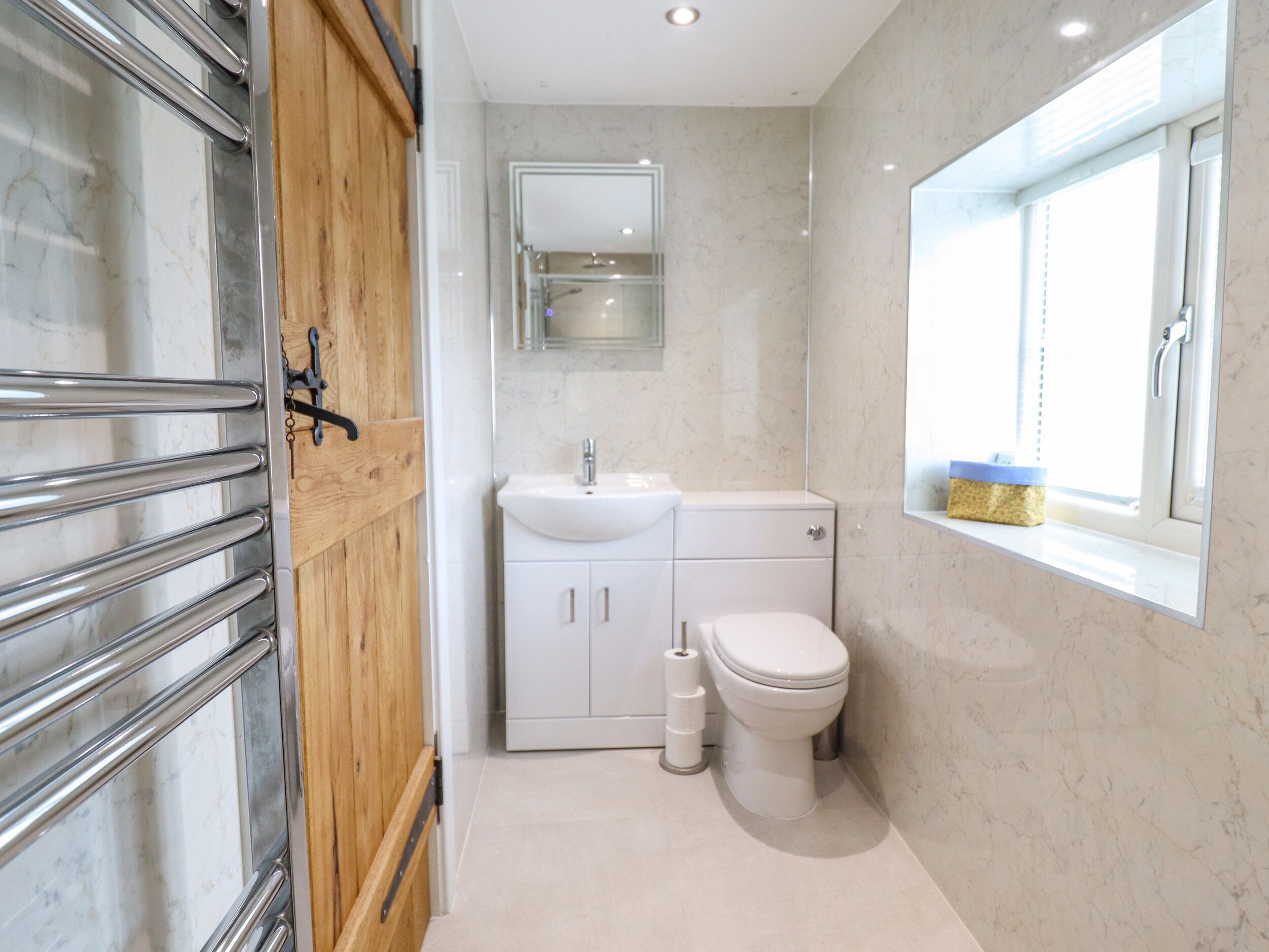 Un bagno con porta in legno, lavandino bianco, WC e finestra vista.