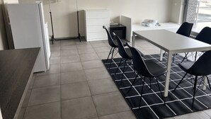 A modern kitchen with a white refrigerator, a small white cabinet, and a black chair at a white table.