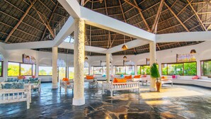 Un hall espacioso con techo alto y tejado de paja, que cuenta con una zona de estar central con cojines de colores y una gran planta en maceta.