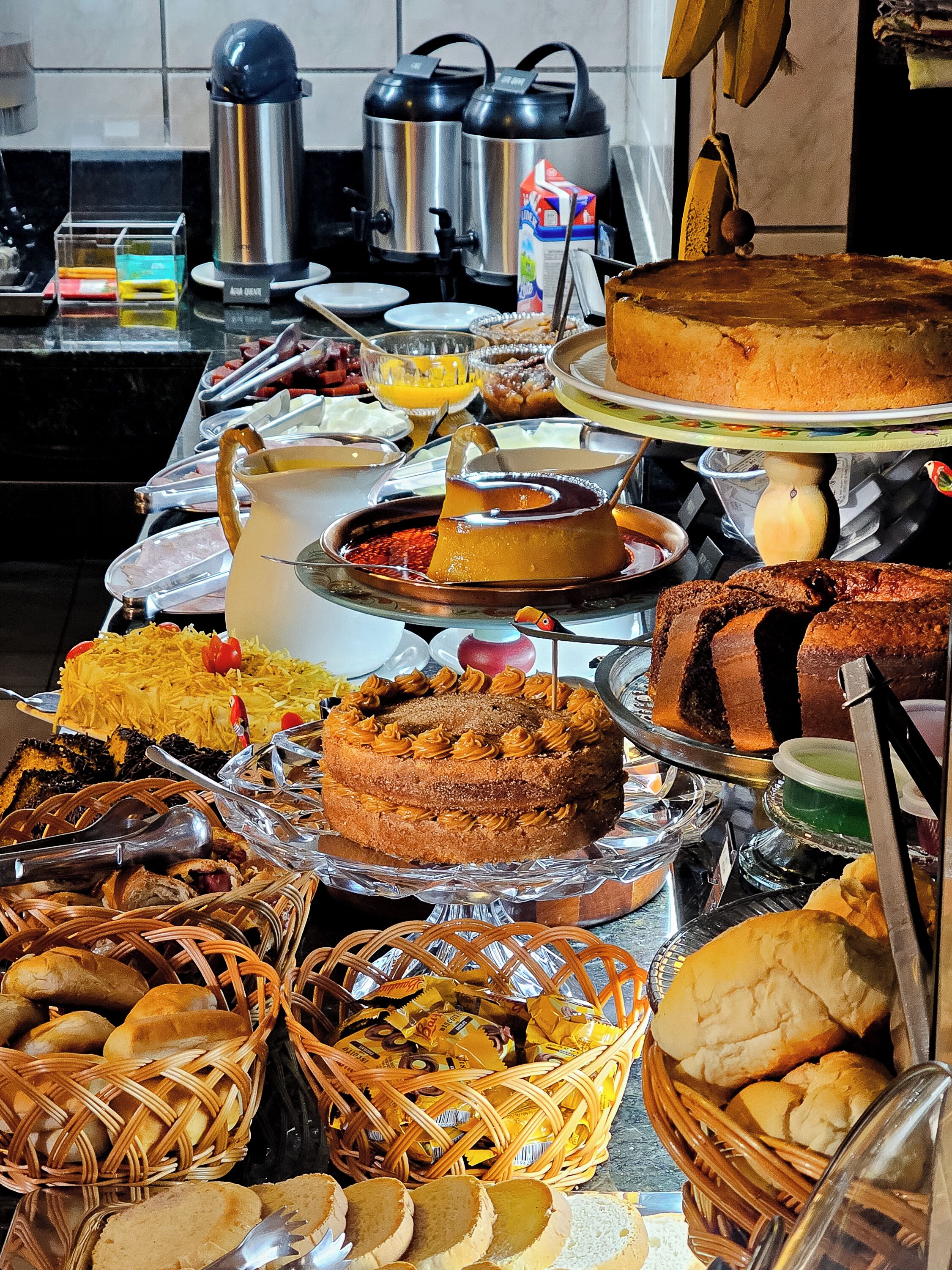 Buffet com diversos pratos, incluindo bolos, doces e uma variedade de opções.