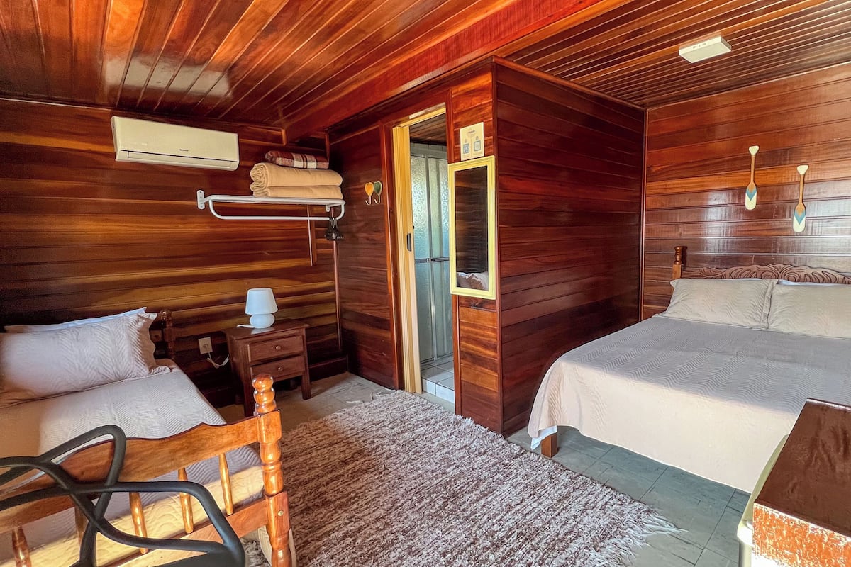 A wooden room with a bed, a chair, a nightstand, a lamp, and a mirror.