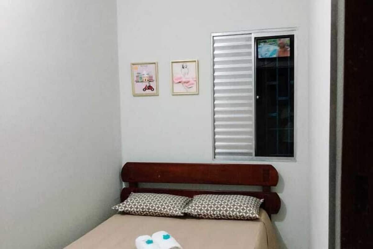 A small, neatly made bed with a wooden headboard, two pillows, and two rolled towels on the bed.