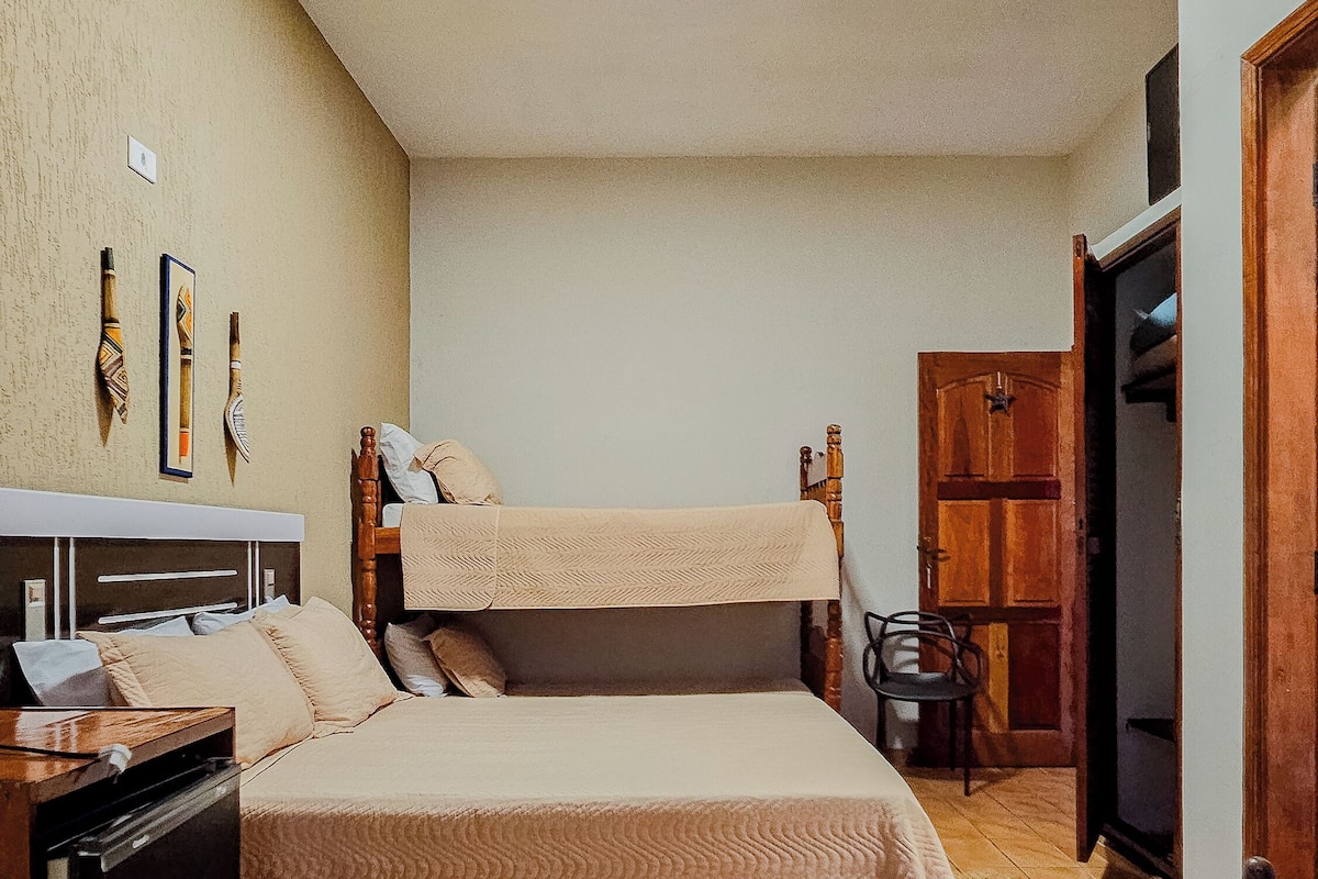 A bedroom with two beds, a wooden wardrobe, a desk with a chair, and a small table.