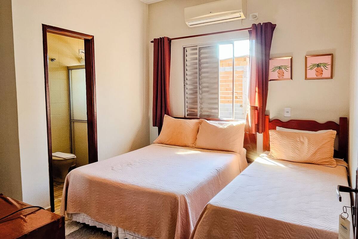 A hotel room with two beds, a bathroom with a mirror, and a window with curtains.