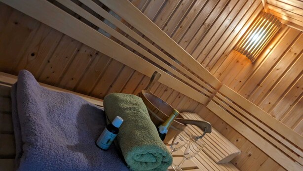 Puuinen sauna, jossa on penkki, pyyhkeet ja pullo öljyä.