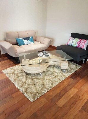 Relax in this stylish living room with a glass coffee table, a beige sofa, and a black sofa with a vibrant cushion.