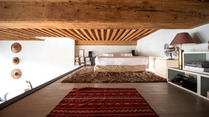 A bedroom with a wooden ceiling, a bed, a red patterned rug, a white wall with circular decorations, and a bedside table with a lamp. - LE LOFT ETHNIC - Grand Studio avec magnifique vue (Lyon)