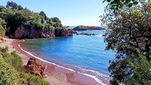 A coastal landscape with a rocky beach, clear blue waters, and lush greenery.