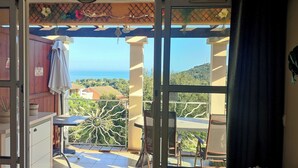 A balcony with a view of the sea, a table, chairs, and a hanging light fixture.