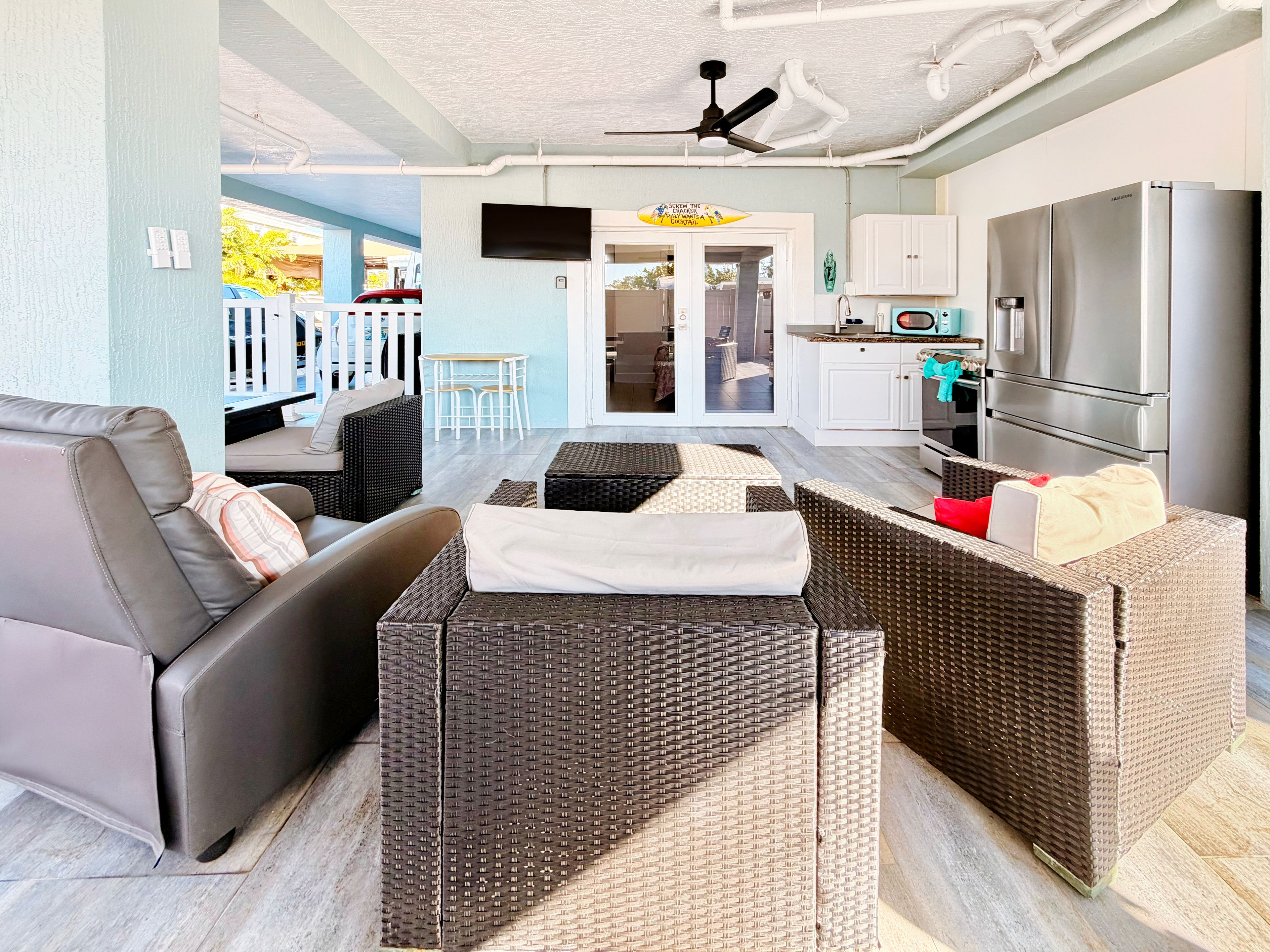 A modern living area with a sofa, wicker furniture, a flat-screen TV, and a kitchen with a refrigerator.