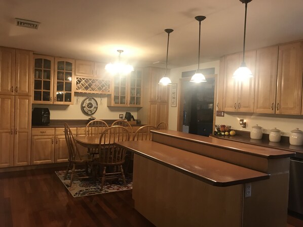 Een keuken met houten kastjes, een centraal eiland met stoelen, hanglampen en een koelkast.