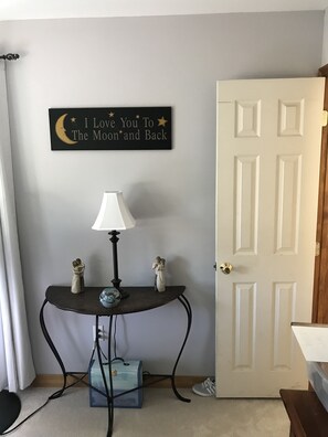 Una habitación con una puerta, un letrero en la pared, una mesa con una lámpara y dos figuritas.