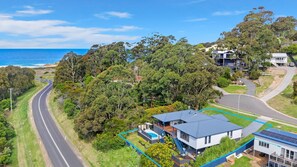 A modern house with a large backyard, a swimming pool, and a view of the ocean.