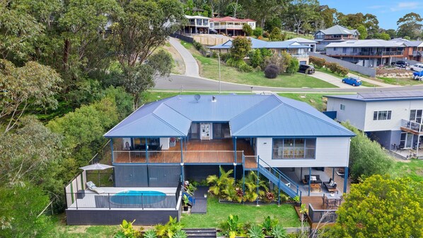 A modern two-story house with a large deck, a swimming pool, and a well-maintained garden.