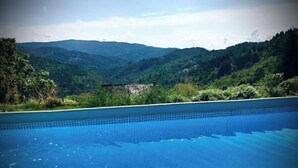 A swimming pool with clear blue water, surrounded by lush greenery and hills in the background.