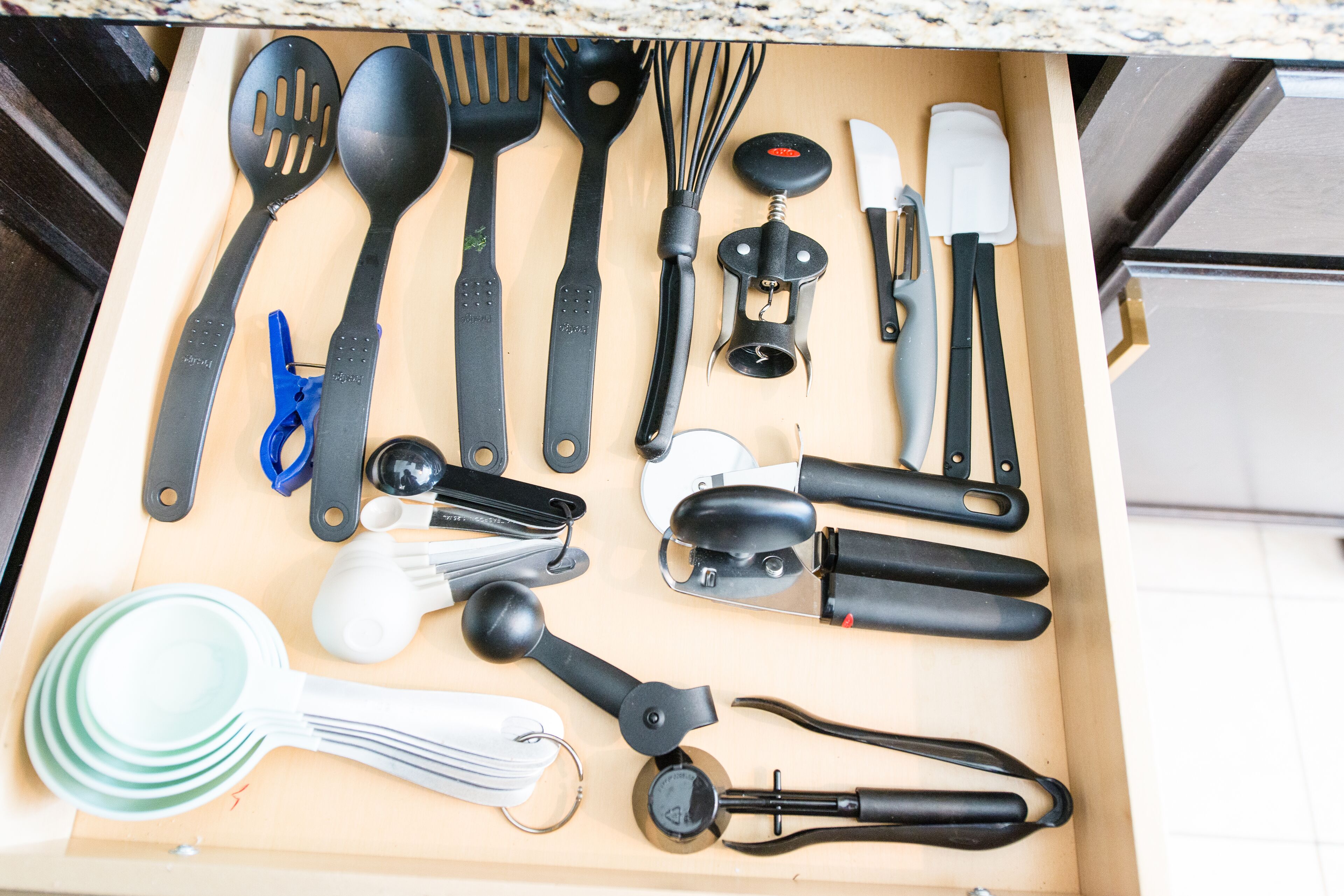 A drawer with various kitchen utensils including spatulas, a whisk, a grater, and a knife.