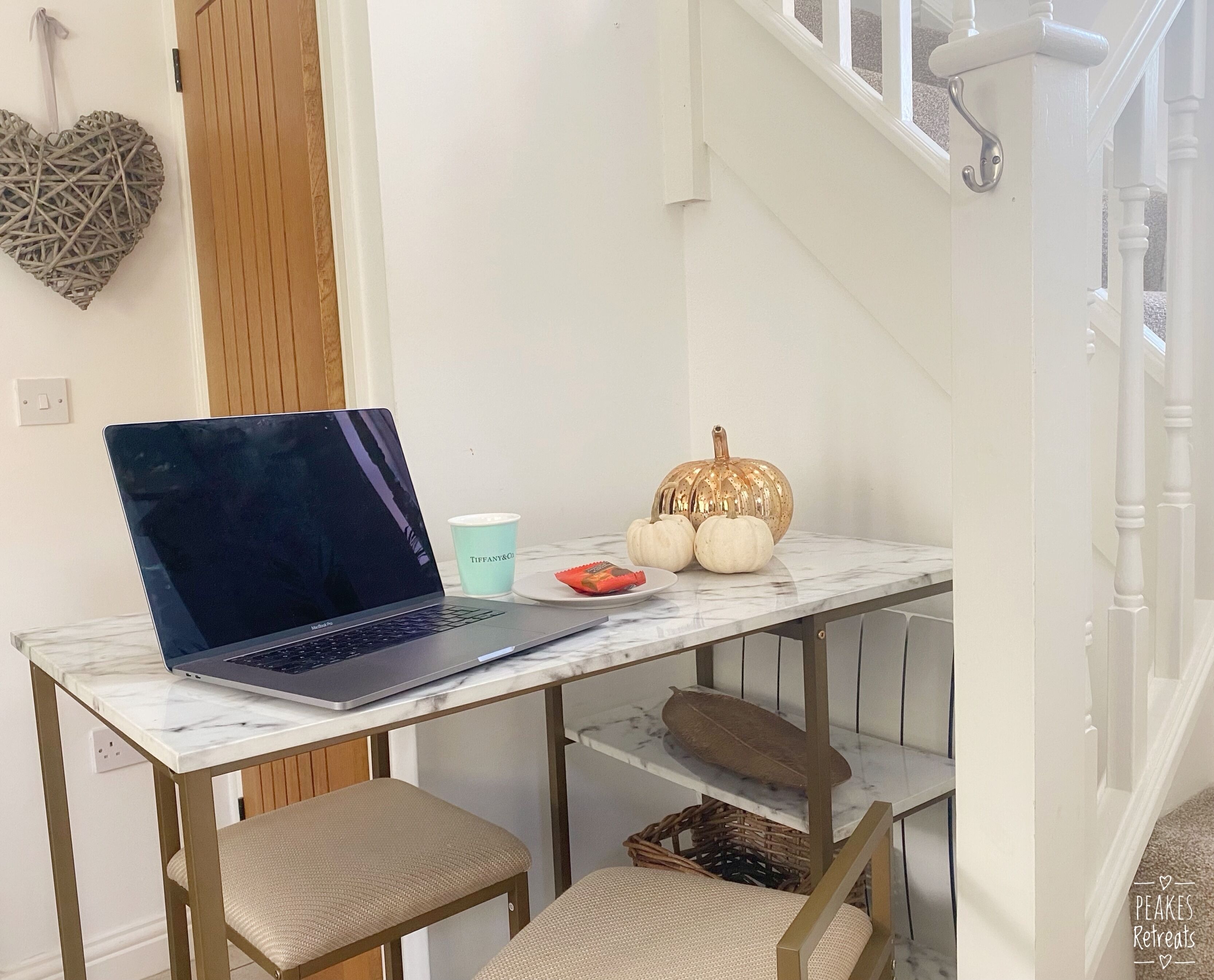 Un ordinateur portable sur une table en marbre, une tasse et des citrouilles décoratives.