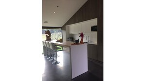 A modern kitchen with a central island, bar stools, and a view of greenery outside. - Villa D'architecte Design au Pied du Luberon (Mérindol)