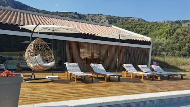 A poolside area with lounge chairs, a hanging chair, and a view of a mountainous landscape. - Villa D'architecte Design au Pied du Luberon (Mérindol)