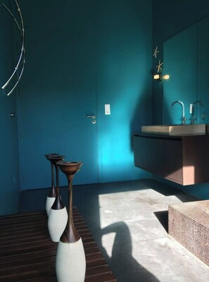 Une salle de bain avec un mur bleu, un lavabo et deux vases posés sur un banc en bois.