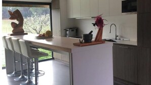 A modern kitchen with a central island, bar stools, and a view of greenery outside. - Villa D'architecte Design au Pied du Luberon (Mérindol)