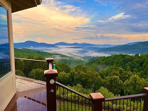 A balcony with a view of a forested valley and distant mountains.