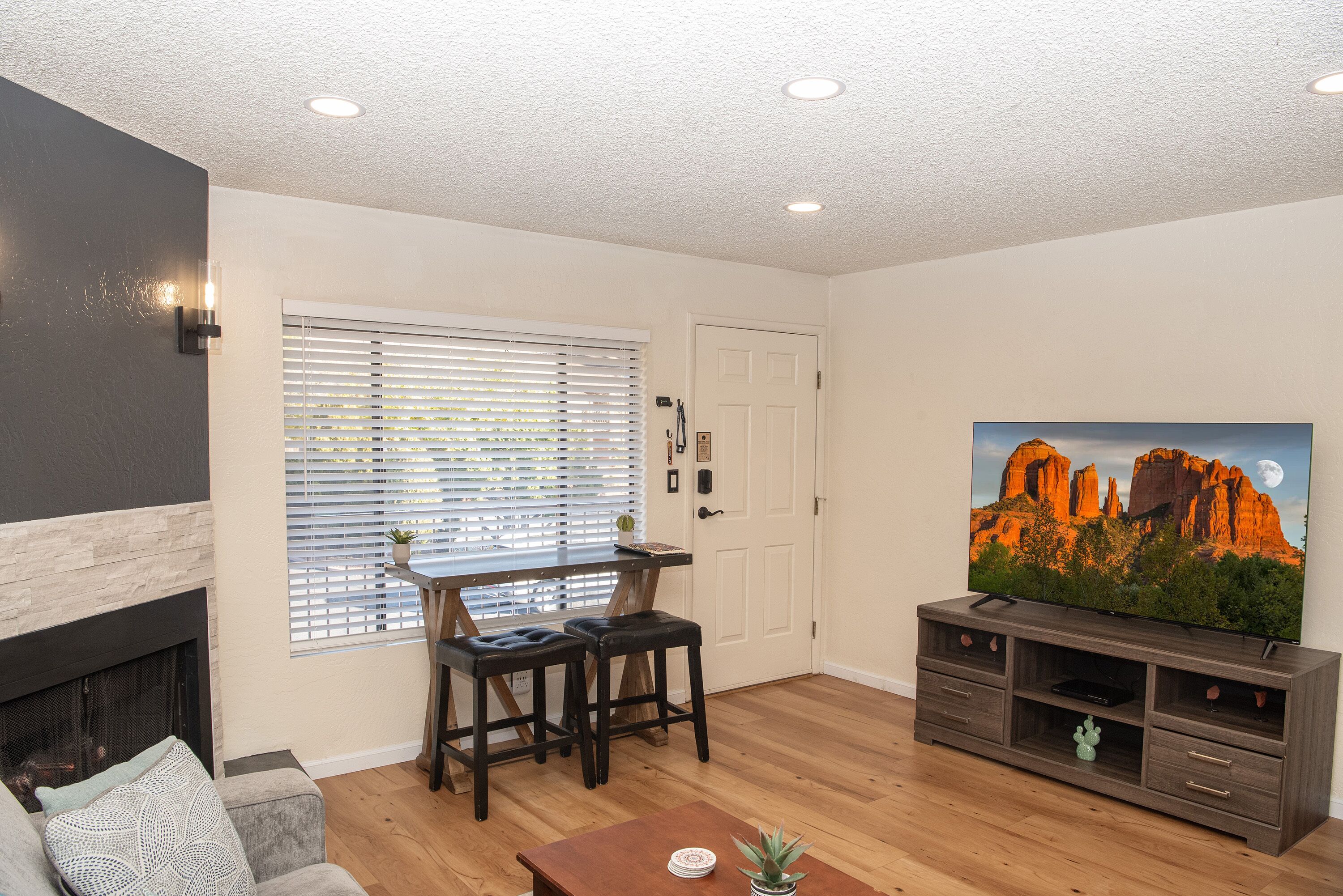 Una sala de estar con chimenea, un comedor con mesa y sillas, un televisor sobre un mueble bajo y una puerta con ventana y persianas.