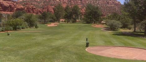 Un campo de golf con vistas despejadas a formaciones rocosas rojas al fondo.