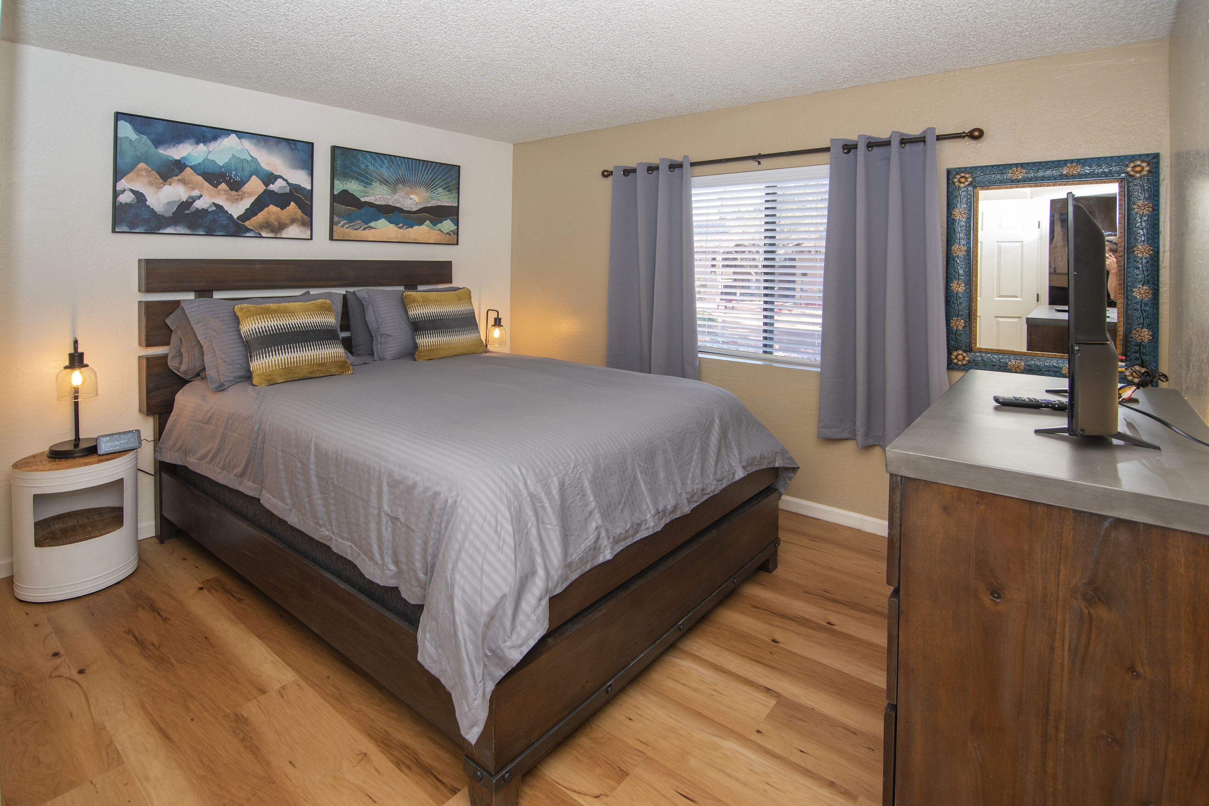 A bedroom with a bed, a nightstand, a dresser, a mirror, and two paintings on the wall.