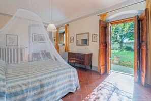 Een slaapkamer met een bed, nachtkastje, kapstok, spiegel en raam met gordijnen.