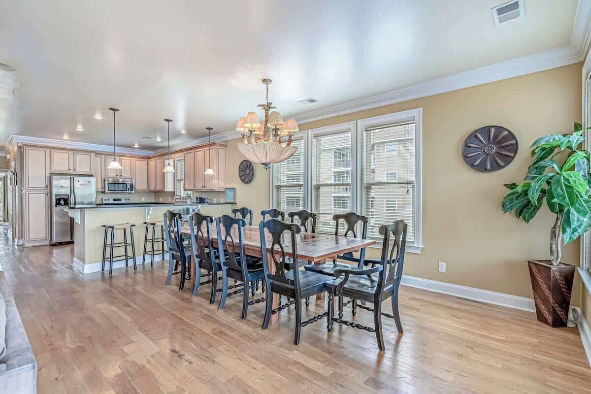 A spacious kitchen with a dining area, wooden flooring, and a large window with blinds.