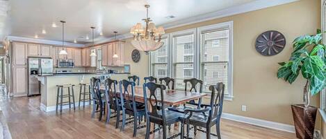 A spacious kitchen with a dining area, wooden flooring, and a large window with blinds.