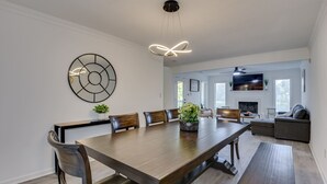A modern dining room with a large wooden table, six chairs, and a decorative wall piece. - Beautiful 3BR Townhouse (Augusta)